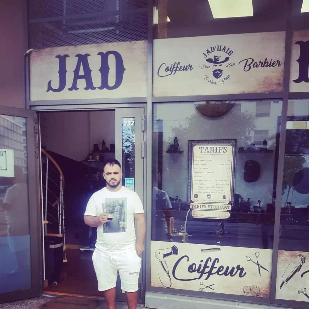 ismail debout devant une boutisque de barbier