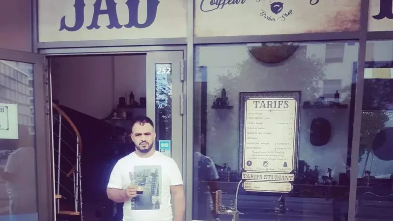 ismail debout devant une boutisque de barbier